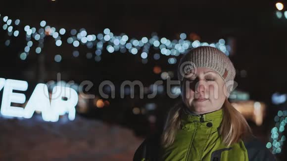 冬天晚上戴帽子的漂亮女人站在圣诞花环的背景下新年夜晚视频的预览图