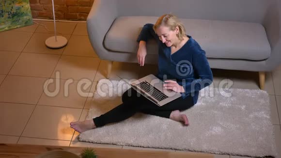 高白种人女性在室内坐在地板上时用手提电脑开心地笑视频的预览图