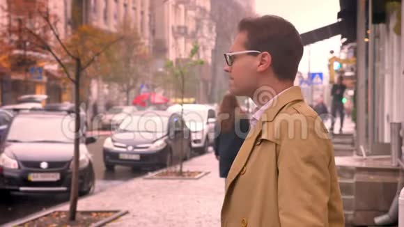 戴眼镜的可爱的白种人站在人行道上寻找一个人检查手表上的时间视频的预览图