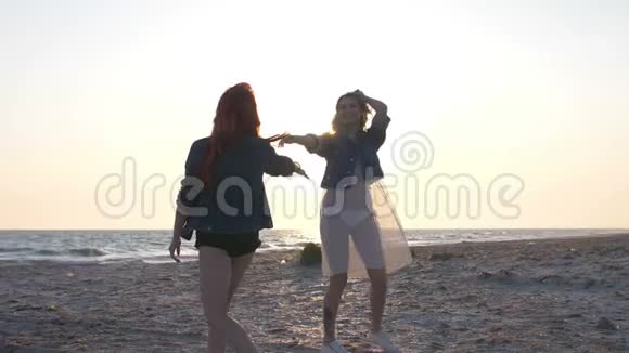 海面上的落日余晖照亮了两个穿着boho风格的年轻性感女人在海滩上的舞蹈视频的预览图