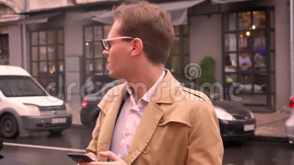 一名戴眼镜的白种人成年男子正在检查街道上的电话等待有关人士的到来视频的预览图