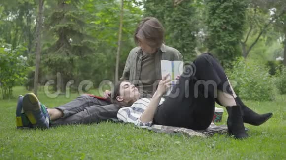 年轻的一对穿着休闲服装的夫妇在户外聚会约会坐在草地上毯子上的人视频的预览图