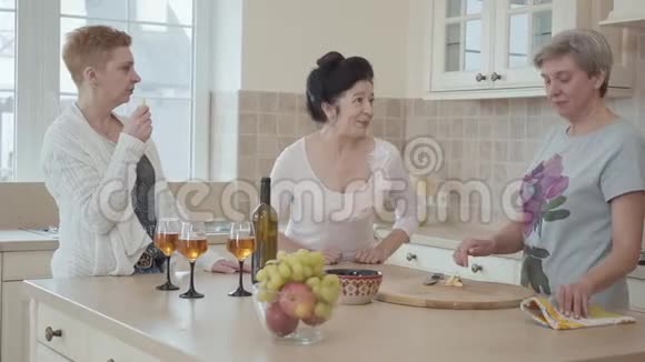 三个成熟的女人在家里交流站在厨房的现代餐桌旁一位讲故事的女士视频的预览图