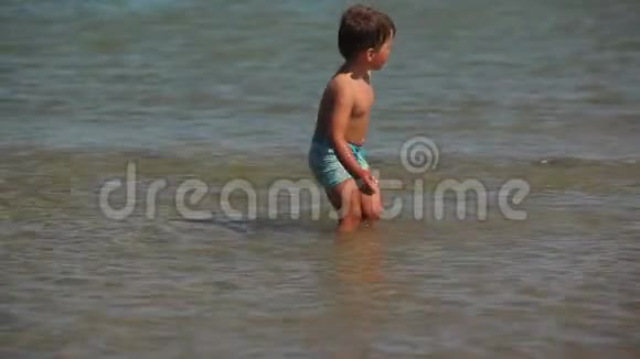 小男孩在沙滩上的水里跑步视频的预览图