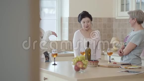 三个在家里交流的成熟女人站在厨房的现代餐桌旁感情用事地讲故事的女士视频的预览图