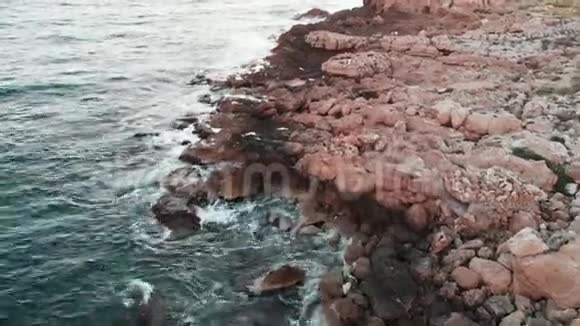 无人驾驶飞机沿海岸与岩石海滩海浪撞击海洋石头的空中景色视频的预览图