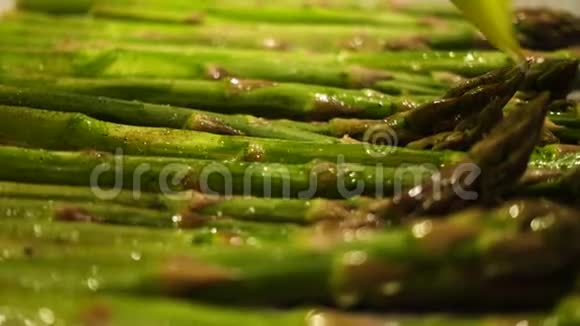 在烤熟前用刷子将新鲜的绿芦笋茎涂上油视频的预览图