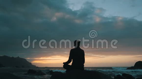 一位妇女坐在岩石上的剪影日落时在加那利群岛特内里费的贝尼霍海滩观察海浪视频的预览图
