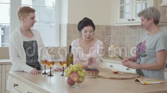 三个中年成熟的女人在家里聊天站在厨房中间的现代桌子附近一个视频的预览图
