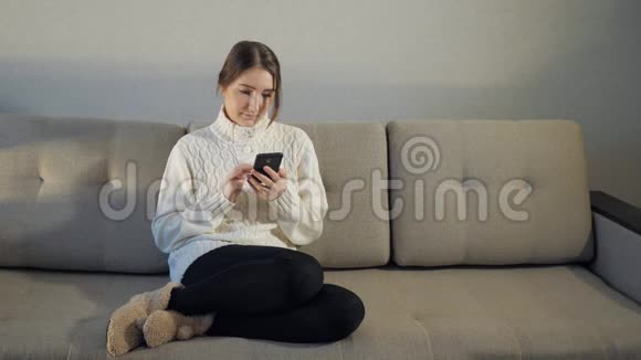 穿毛衣的漂亮女孩坐在沙发上看电话留言视频的预览图