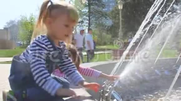 穿条纹夹克的女孩在城市公园的喷泉里玩水视频的预览图