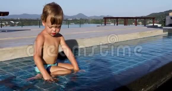 小男孩坐在岸上把石头扔到户外的水里视频的预览图