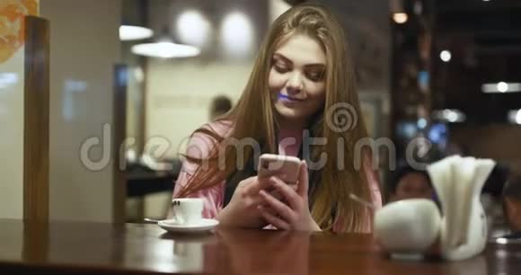 穿着玫瑰毛衣的年轻女子手里拿着智能手机一边在客厅里聊天一边在屏幕上打字视频的预览图