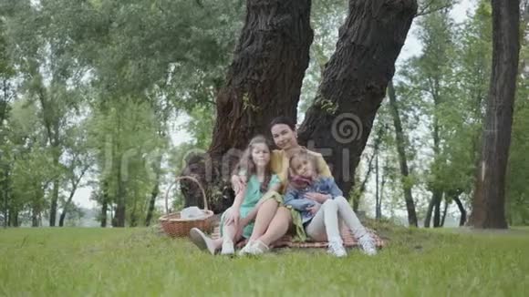 公园里一位可爱的老太太坐在树下的草地上亲吻和拥抱可爱的孙女视频的预览图