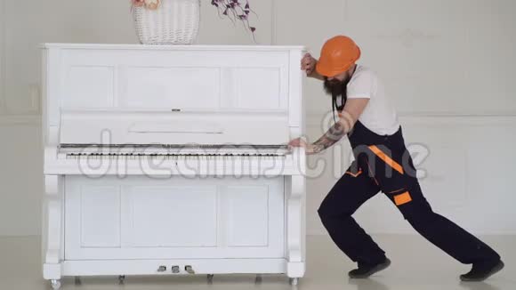 男人带着胡子工人戴着头盔穿着工作服努力移动钢琴装载机移动钢琴乐器一个男人视频的预览图