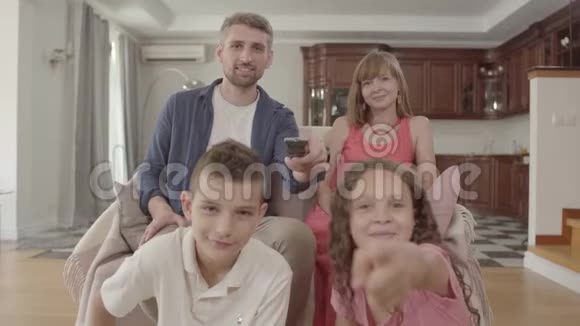肖像年轻家庭一起坐在家里看电视父亲拿着遥控器打开频道视频的预览图