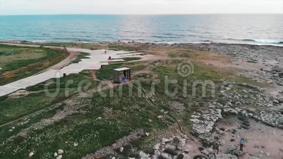 Drone乘坐飞机穿过狭窄的旅游人行长廊人们在岩石海滩上放松地平线上有海洋视频的预览图
