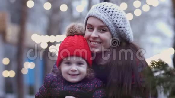 一位年轻的母亲抱着她的小女儿坐在长凳上看着相机一个幸福的家庭灯光亮着视频的预览图