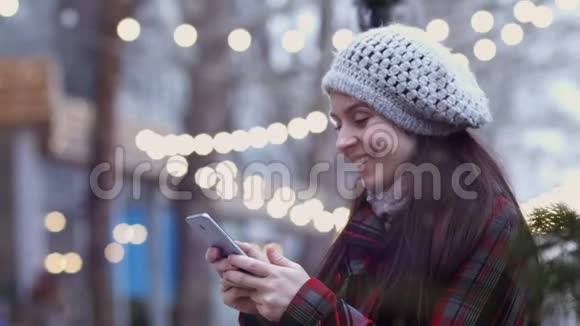 心情愉快的年轻快乐女子戴着贝雷帽坐在城市长凳上用手机发短信读着好消息视频的预览图