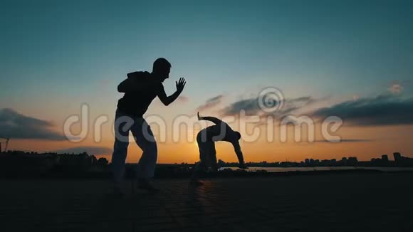 两名运动员的剪影他们在夏日日落的背景下跳巴西卡波埃拉舞视频的预览图
