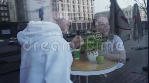 从街上的玻璃窗拍到一个年轻的uy和女孩在咖啡桌上约会恋爱中的年轻夫妇视频的预览图