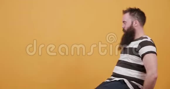 一个留胡子的年轻人在黄色背景前的旋转椅子上玩视频的预览图