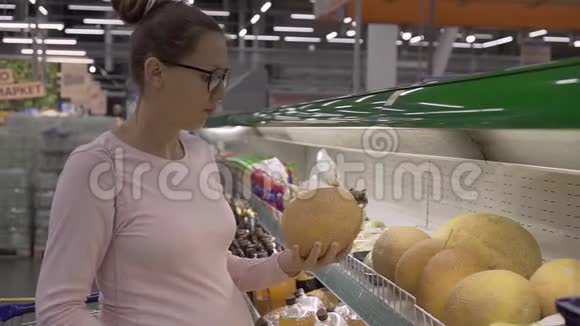 在超市里戴眼镜的年轻孕妇选择新鲜的有机水果女人在购物时选择水果视频的预览图
