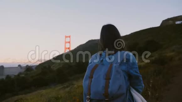 镜头跟随年轻的旅游妇女背包徒步上大山欣赏壮观的金门大桥日落景色视频的预览图