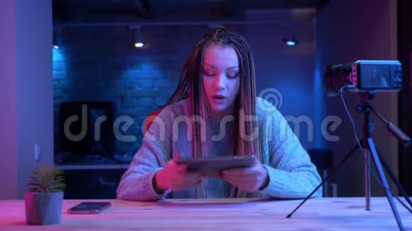 年轻有魅力的女性博客写手在平板电脑上发短信的特写镜头与霓虹灯一起直播视频的预览图