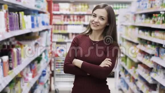 美丽的女人站在超市的货架之间微笑着看着摄像机视频的预览图