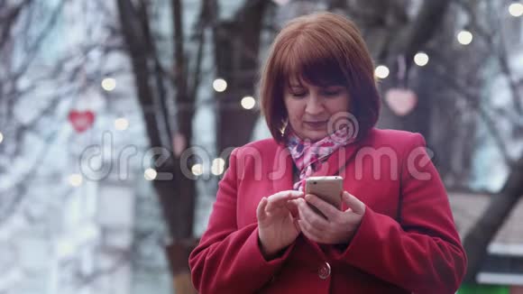 微笑的成年女性使用智能手机在公园放松背景灯慢动作视频的预览图