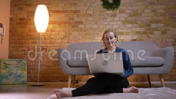 白种人年长女性坐在地板上兴奋地在笔记本电脑上看电影的特写镜头视频的预览图