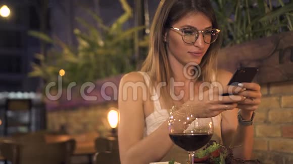 年轻女性食品博客写手在优雅的咖啡馆吃饭时拍照漂亮的女人用手机坐在桌子旁视频的预览图
