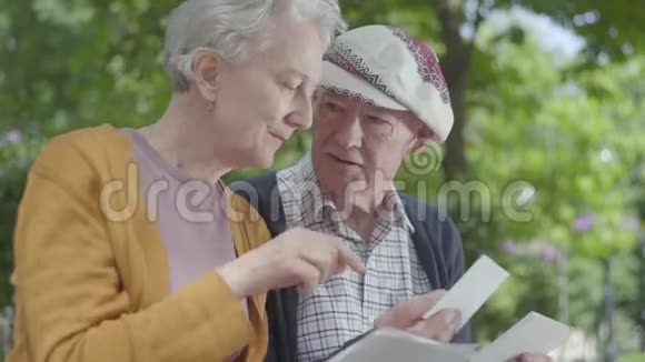 特写肖像可爱的成熟夫妇看着老照片回忆着坐在公园长凳上的快乐时刻视频的预览图