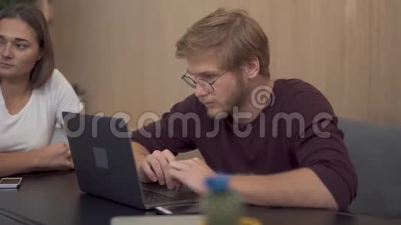 一个坐在笔记本电脑旁的留胡子的年轻人正在仔细地听财务报告商务人士会议视频的预览图