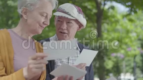 特写肖像可爱的成年夫妇看着老照片回忆着坐在公园长凳上的快乐时刻视频的预览图
