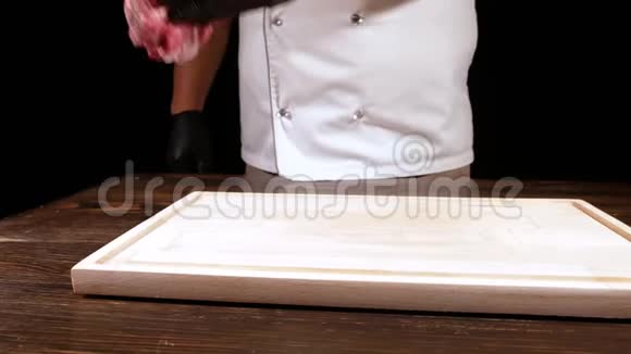 一个穿白色围裙的厨师把一块生肉放在木板上盐季节然后把它带到一边视频的预览图