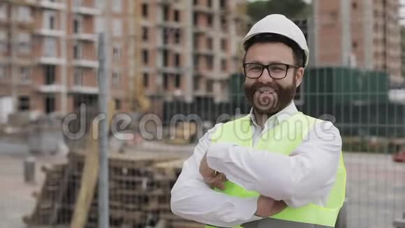 微笑的建筑师站在建筑工地上交叉双手看着摄像机的肖像外部视频的预览图