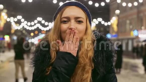 一个可爱的年轻女孩的肖像长着一头金色的长发站在一条喜庆的城市街道上穿着一件冬天的夹克闪闪发光视频的预览图