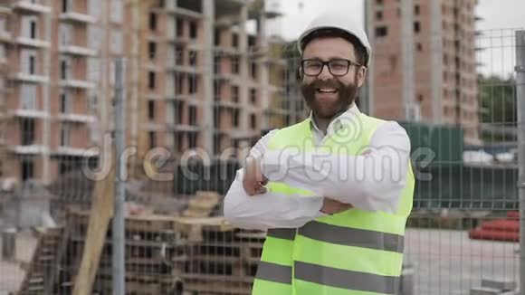 微笑的建筑师站在建筑工地上交叉双手看着摄像机的肖像外部视频的预览图