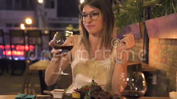 美丽的女人在烧烤餐厅晚餐时喝着酒杯里的红酒年轻女子喝葡萄酒视频的预览图