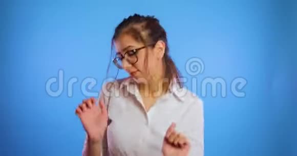 穿着白色衬衫的年轻滑稽的黑发女人在蓝色背景下跳舞微笑着视频的预览图