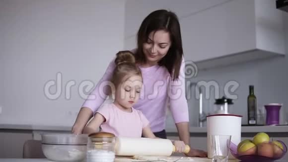 白人年轻慈爱的母亲快乐地帮助她可爱的小女儿用擀面杖擀面视频的预览图