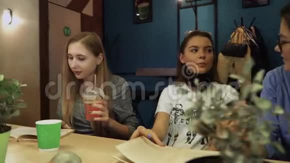 三个女朋友一边聊天一边坐在咖啡馆的一张桌子上看书年轻人健康的生活方式视频的预览图