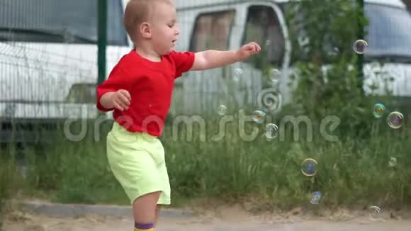 一个小男孩在模糊的汽车背景上捕捉肥皂泡慢动作视频的预览图