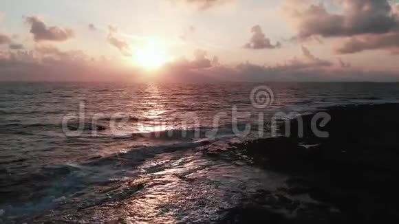 壮丽的粉红色日落的空中拍摄阳光和巨大的海浪撞击岩石海滩视频的预览图