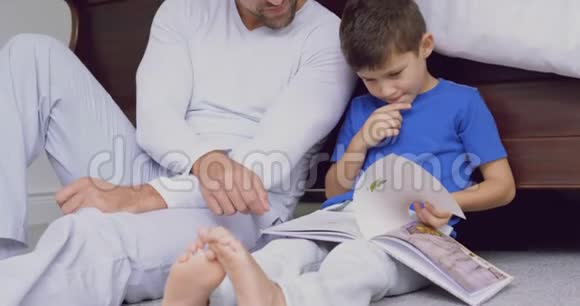 父亲和儿子在舒适的家里卧室里读故事书视频的预览图