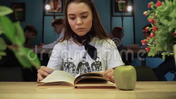 年轻严肃的女孩专注于在其他游客的背景下在咖啡馆里读一本教科书视频的预览图