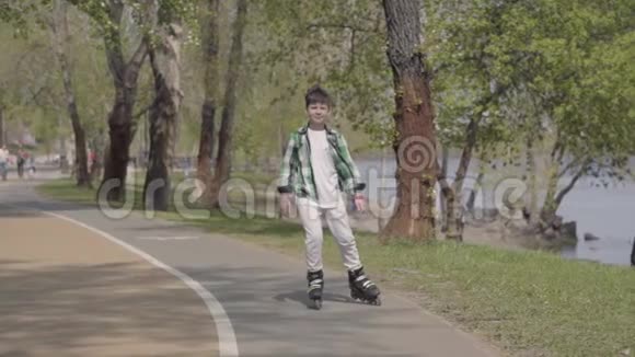 可爱的男孩穿着鲜艳的衣服在河边的公园里滑旱冰户外休闲一个人玩得开心慢慢视频的预览图