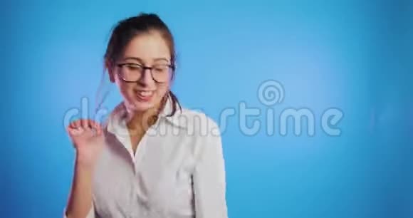 快乐微笑的年轻女孩在蓝色背景下独自跳舞学生快乐表情视频的预览图